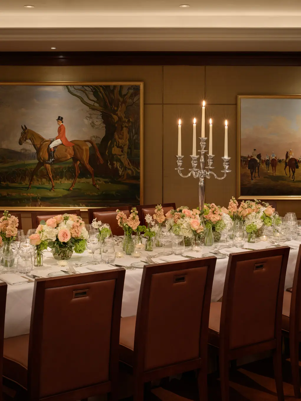 A room with two pictures of horses and a dining table decorated for a wedding with candles and flowers