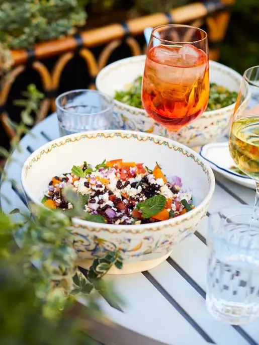 A table filled with two bowls of salad, a glass of white wine and an orange cocktail